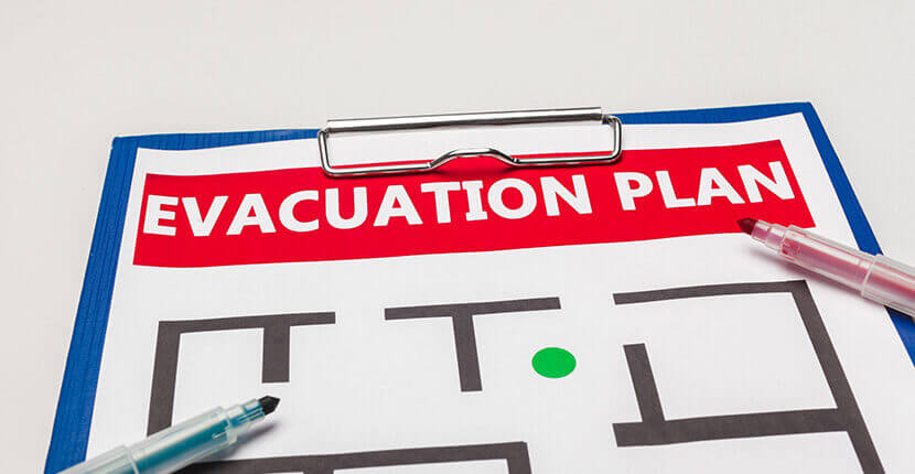 Evacuation plan on a clipboard laying on a surface with two open pens on top.